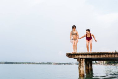 İki kız gölde köprüden atlıyor.