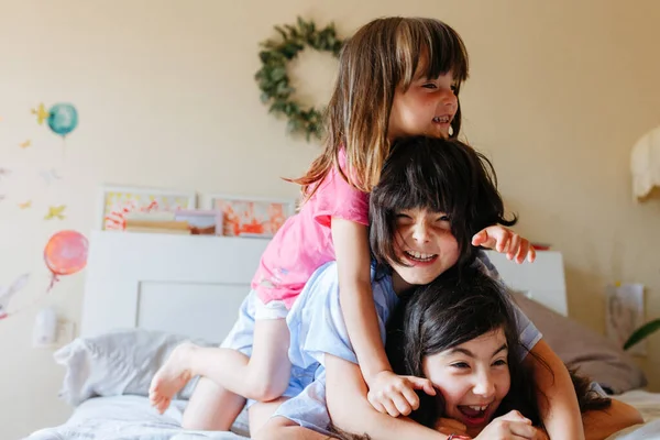 pyramid of three smiling children lying on each other on the bed