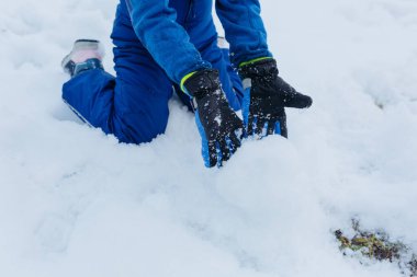 Mavi kışlık pantolonlu, karla oynayan çocuğun eldivenleriyle ellerini kapat.