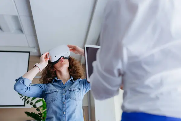 low angle view on woman with curly brown hair and denim shirt trying on VR in the office
