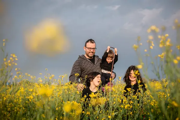 Kids playing next to the father standing in a field with blooming yellow flowers