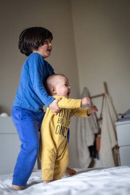 İkisi yatakta mavi ve sarı elbiseli çocuklar ailelerinin gelişini izliyorlar.