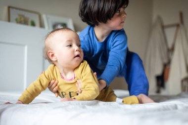 Pijamalı iki gülümseyen kız kardeş ebeveynin yatağında oynuyorlar.
