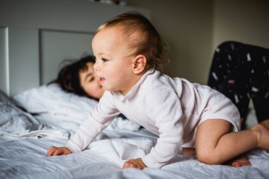 Anne babasının yatağında oynayan pijamalı iki kız kardeşin yan görüntüsü.