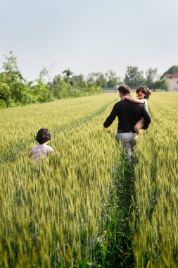 Yeşil buğday tarlasında yürüyen iki çocuklu bir adam.