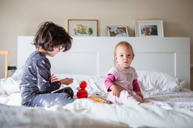 Pijamalı iki kız kardeş aile yatağında oynuyorlar.