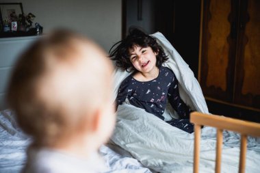 Pijamalı iki kız kardeş aile yatağında oynuyorlar.