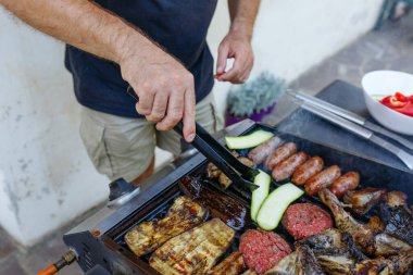 Yakından bakınca insan elleri ızgarada sebze ve et pişiriyor.