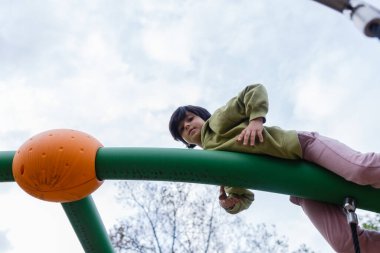 Yeşil elbiseli kızın oyun parkında çapraz çubukta asılı görüntüsü düşük açılı.