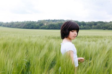 Buğday tarlasında duran, kısa siyah kısa saçlı, beyaz saçlı sakin bir kız.