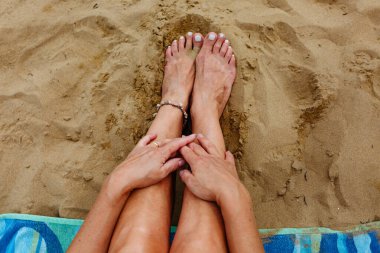 Kadının üst görünüşü ellerini kumlu sahilde bacaklarının üstüne koyuyor.