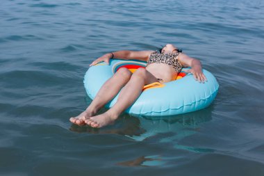 Koyu saçlı çocuk, Garda Gölü 'nün güneşli bir gününde açık mavi şişme yüzüğün üzerinde uzanarak rahatlıyor.