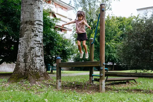 Çocuk parkındaki ahşap banktan atlayan mutlu çocuk.