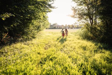 Açık arazide güneşe doğru koşan üç çocuğun arka görüntüsü