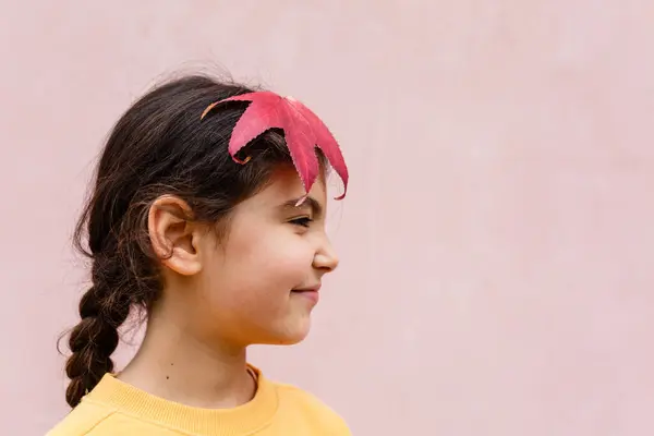 stock image portrait of smiling girl with big red leaf in her hair against pink wall