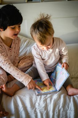 İki küçük kız kardeş evde yatakta oturup kitap izliyorlar.