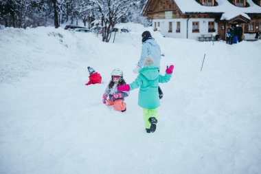Üç çocuklu bir kadın büyük bir evin önünde karda oynuyordu.