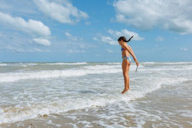 Saçı örgülü, dalgalarla oynayan bir kızın yan görüntüsü.