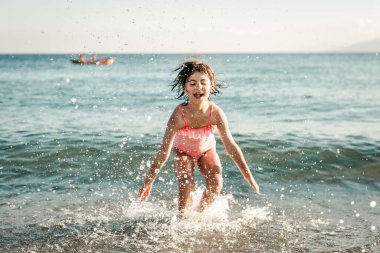 Çizgili mayo giymiş deniz suyuyla oynayan bir kız.