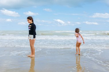 Saçları örgülü iki kız güneşli bir günde denizde dalgalarla oynuyorlar.