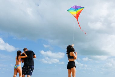 Gökyüzüne karşı duran güneşli bir günde gökkuşağı uçurtması uçuran iki kızı olan babanın dikiz görüntüsü