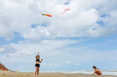 Kumsalda uçurtma uçurup kumla oynayan iki çocuğun alçak açılı görüntüsü.