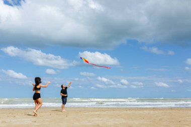 Güneşli bir günde denizin kenarında gökkuşağı uçurtması uçuran baba ve çocuğun geniş açılı görüntüsü.