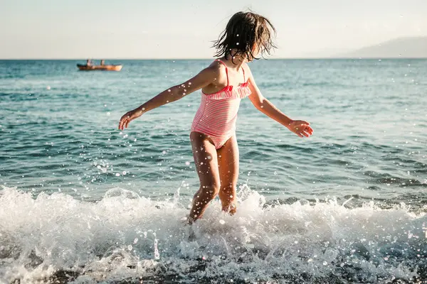 Çizgili mayolu küçük kız denizde dalgalarla oynuyor.