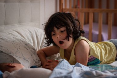 Uykulu küçük çocuk evde yatağında yeni doğan kardeşine bakıyor.