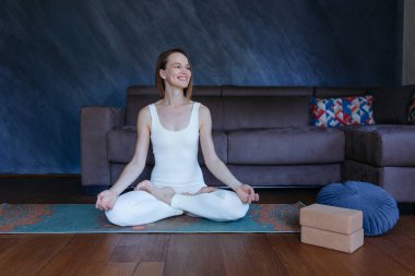 Padmasana yogasında oturan kadın evinde kanepenin önünde egzersiz yapıyor.