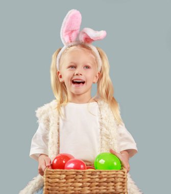 Paskalya yumurtaları ve gri arka planda tavşan kulaklı tatlı mutlu kız, paskalya kompozisyonu, elinde paskalya yumurtası tutan çocuk, dini bayram konsepti, bahar havası, boş alan, izole edilmiş çocuk..