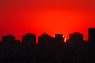 Günbatımında kızıl gökyüzü olan modern bir şehrin silueti.