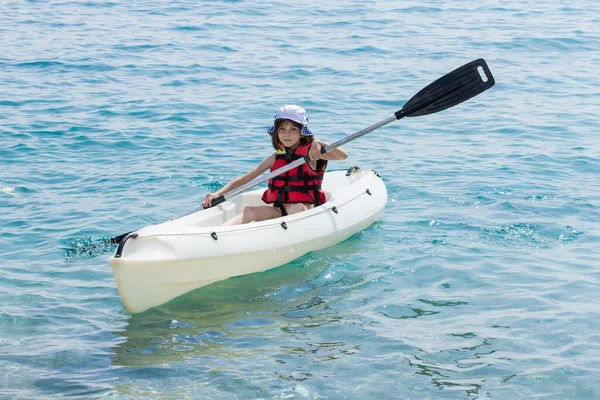 Beautiful girl in a life jacket on a canoe boat. The child holds the sail on a boat. Swimming on the sea. Children's sports.