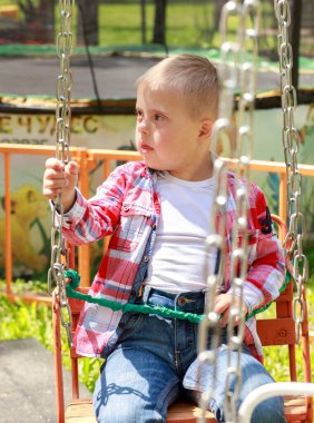 Parkta Down Sendromlu bir çocuk var. Yeşilliğin arka planına karşı. Çocuk gülümsüyor.