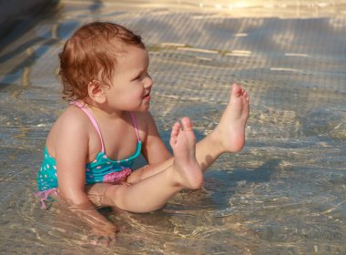 Mavi mayolu bir kız çocuk havuzunda mayo giyip oynuyor. Çocuk yüzmeyi öğreniyor. Yaz aktif açık hava oyunları.