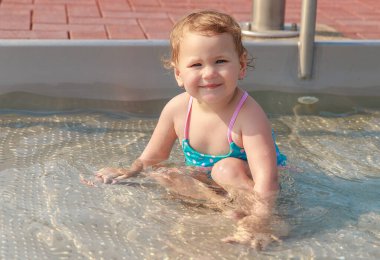 Mavi mayolu bir kız çocuk havuzunda mayo giyip oynuyor. Çocuk yüzmeyi öğreniyor. Yaz aktif açık hava oyunları.