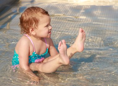 Mavi mayolu bir kız çocuk havuzunda mayo giyip oynuyor. Çocuk yüzmeyi öğreniyor. Yaz aktif açık hava oyunları.