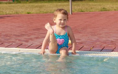 Mavi mayolu bir kız çocuk havuzunda mayo giyip oynuyor. Çocuk yüzmeyi öğreniyor. Yaz aktif açık hava oyunları.