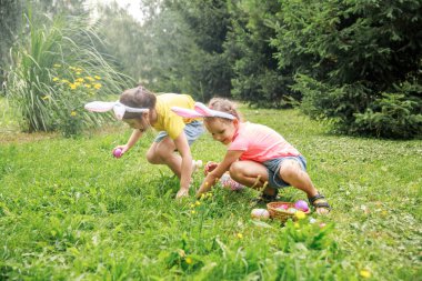 Küçük tatlı kızlar çimenlerde paskalya yumurtası toplarlar. Paskalya tavşanı kulaklı tavşan kostümlü çocuklar. Kızlar otların arasında paskalya yumurtası arıyorlar. Çocuklar dışarıda..