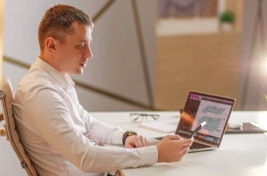 Bir iş adamı ofiste büyük bir masada dizüstü bilgisayarın önünde oturur ve internette çalışır, görüntülü konuşma, internette çalışma anları üzerine iletişim, ofisten çalışma, uzaktan çalışma kavramı..