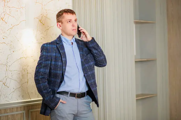 Portrait of a man in a suit. The man speaks on the phone. Important business negotiations. Office worker, sales manager, head of sales department. Serious man adjusts the sleeve of his jacket.