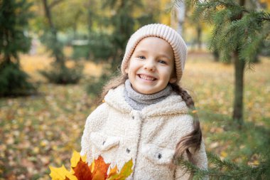 Sonbaharda güzel bir kızın portresi. Ağaçlarda turuncu ve sarı yapraklar. Ekim. Çocuklarla parkta bir yürüyüş..