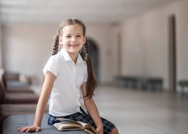 Okula dönersek, birinci sınıftan bir kız ders aralarında okul koridorunda oturuyor. Kız hevesle bir okul kitabı okuyor. İlkokulda kitap okuyordum..