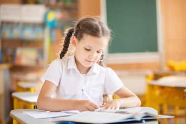 Okula geri dönmek, sınıftaki okul masasında oturan bir kız. Liseli bir kız ders veriyor ve bir deftere yazıyor. Okul malzemeleri çocukların masasında. Kız okul üniforması giyiyor..