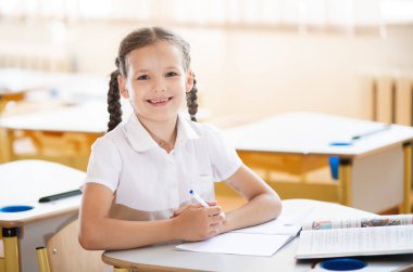 Okula geri dönmek, sınıftaki okul masasında oturan bir kız. Liseli bir kız ders veriyor ve bir deftere yazıyor. Okul malzemeleri çocukların masasında. Kız okul üniforması giyiyor..