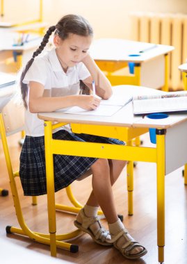 Okula geri dönmek, sınıftaki okul masasında oturan bir kız. Liseli bir kız ders veriyor ve bir deftere yazıyor. Okul malzemeleri çocukların masasında. Kız okul üniforması giyiyor..