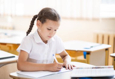 Okula geri dönmek, sınıftaki okul masasında oturan bir kız. Liseli bir kız ders veriyor ve bir deftere yazıyor. Okul malzemeleri çocukların masasında. Kız okul üniforması giyiyor..