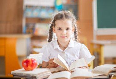 Şirin bir kız ders sırasında bir sınıfta oturuyor ve ders kitabının sayfalarını karıştırıyor. Kız kitap okuyor. Çocuk birinci sınıfa gidiyor. Kız dersini alıyor..