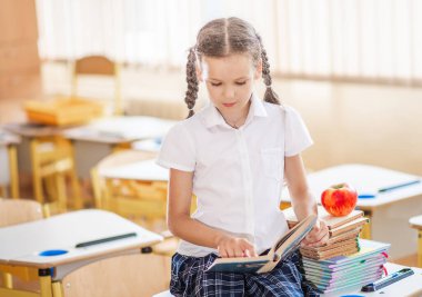 Okula dönecek olursak, birinci sınıf öğrencisi bir kız ders sırasında bir okul masasında otururken kitap okur. Bir liseli kız ders kitaplarını kullanarak ders çalışıyor. Okul malzemeleri bir çocuğun masasında..
