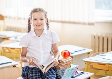 Okula dönecek olursak, birinci sınıf öğrencisi bir kız ders sırasında bir okul masasında otururken kitap okur. Bir liseli kız ders kitaplarını kullanarak ders çalışıyor. Okul malzemeleri bir çocuğun masasında..